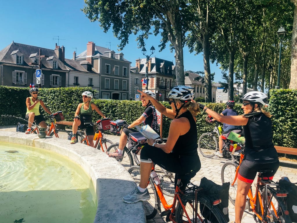 Ciclisti su biciclette arancioni "Girolibero" fermi accanto a una fontana in una piazza con alberi, Francia, Loira